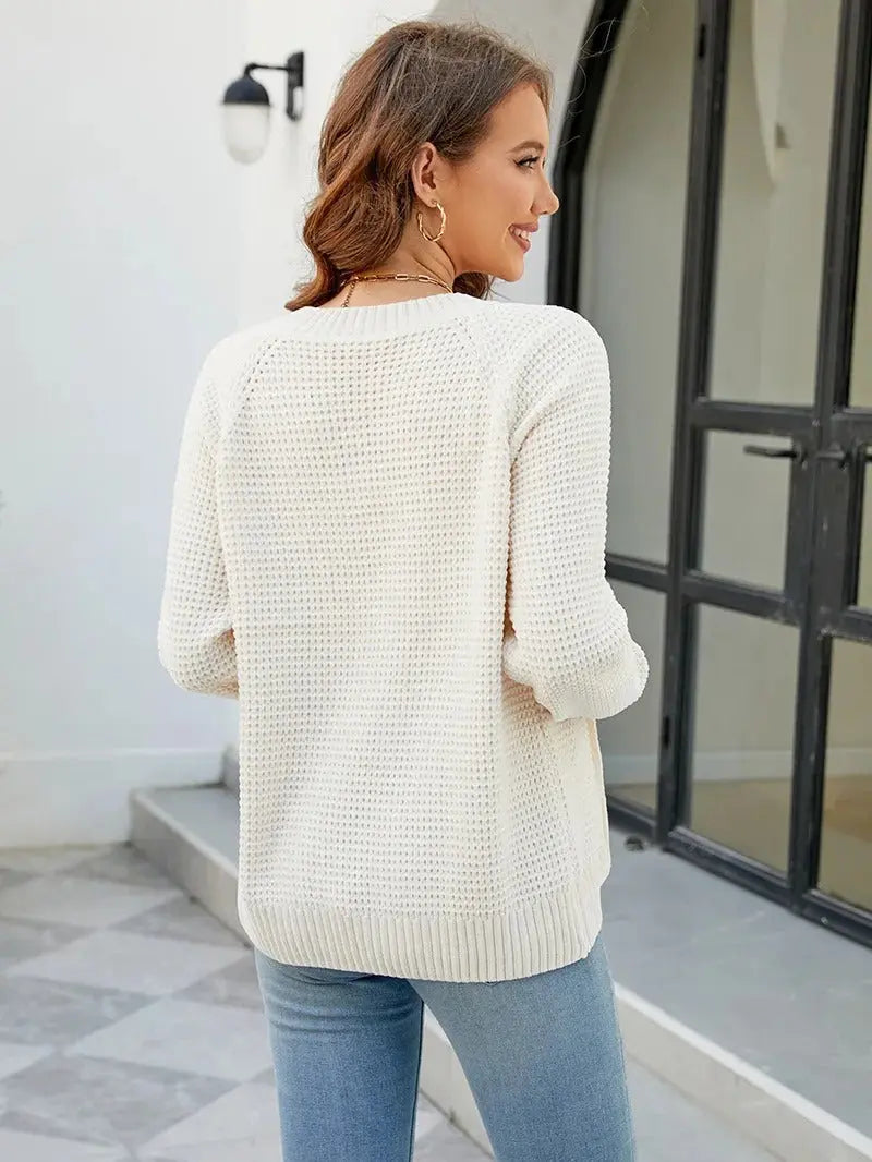 Donna con maglione bianco lavorato a maglia, maniche lunghe, davanti a porta nera. Moda autunnale, abbigliamento casual elegante.