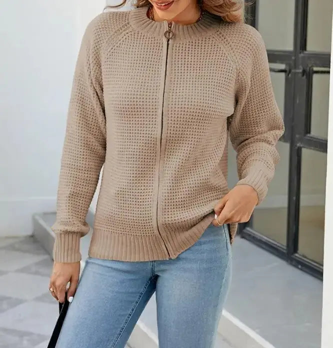 Donna con maglione beige a maglia con zip, jeans blu chiaro, posa casual. Moda autunnale, abbigliamento femminile elegante e confortevole.