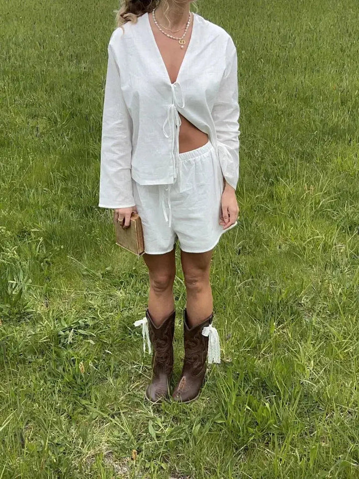 Donna in abito bianco estivo con stivali da cowboy marroni su prato verde. Moda casual, look estivo, abbigliamento femminile trendy.
