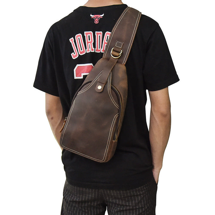Zaino a tracolla in pelle marrone su uomo con maglietta nera. Design elegante, ideale per viaggi e uso quotidiano. Accessorio moda maschile.