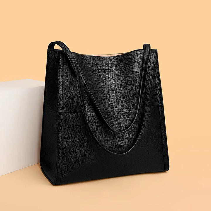 Borsa tote in pelle nera su sfondo beige, design elegante e spazioso, ideale per moda donna, accessori di lusso, shopping e lavoro.