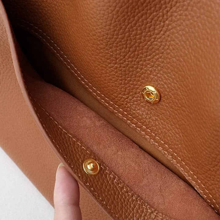 Borsa in pelle marrone con chiusura a bottone dorato, texture granulosa, design elegante e moderno. Accessorio moda donna di alta qualità.