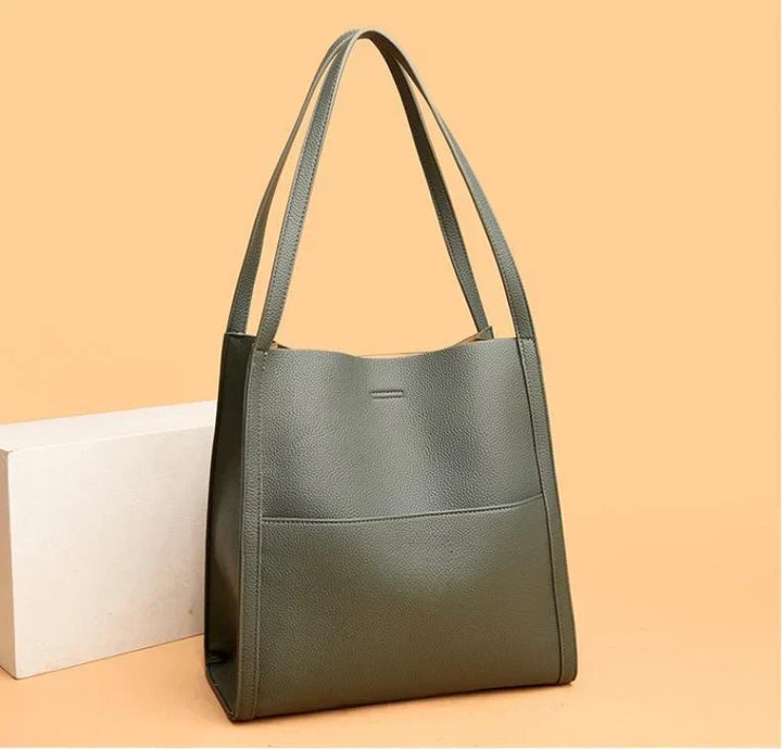 Borsa a spalla in pelle verde oliva, design minimalista, tasca frontale, manici lunghi, sfondo beige. Accessorio moda elegante e versatile.