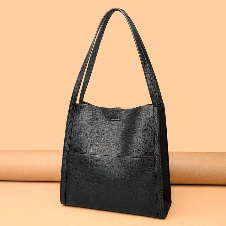 Borsa a spalla in pelle nera elegante su sfondo beige, design minimalista, ideale per moda donna, accessorio versatile e di tendenza.
