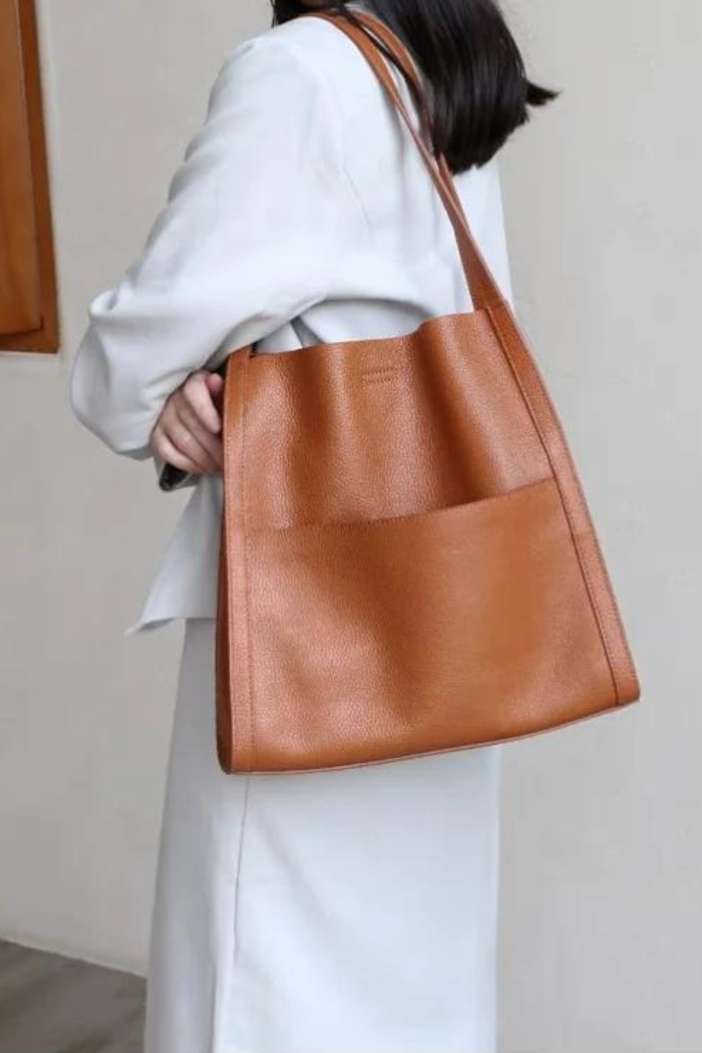 Borsa a spalla in pelle marrone, design elegante e minimalista, indossata da una donna in abito bianco. Accessorio moda femminile di tendenza.