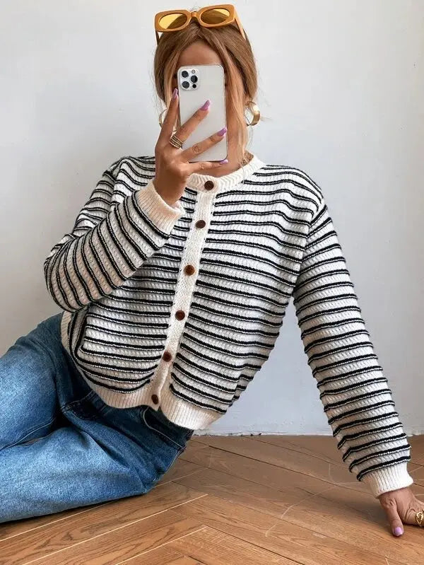 Donna con cardigan a righe bianche e nere, jeans blu, occhiali da sole gialli, scatta selfie con smartphone. Moda casual autunnale.