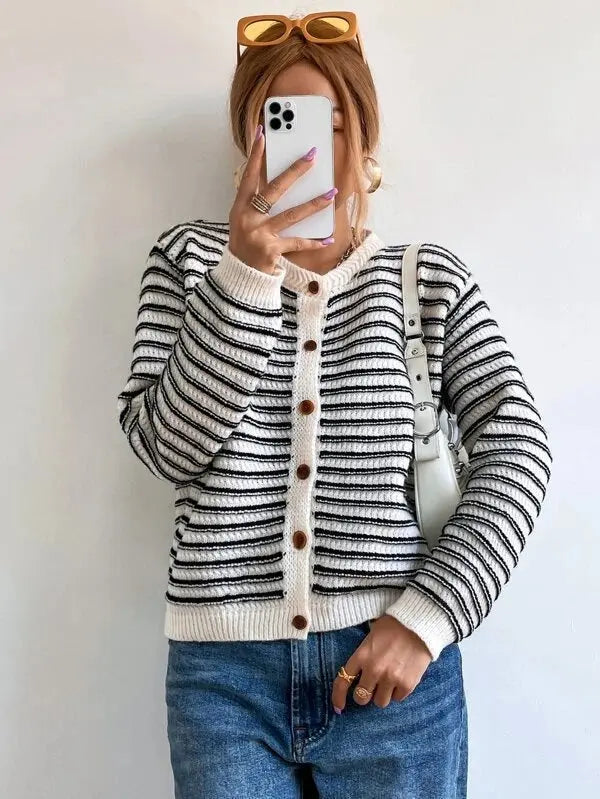 Donna con cardigan a righe bianche e nere, jeans blu, borsa bianca e occhiali da sole marroni. Scatta un selfie con smartphone bianco.