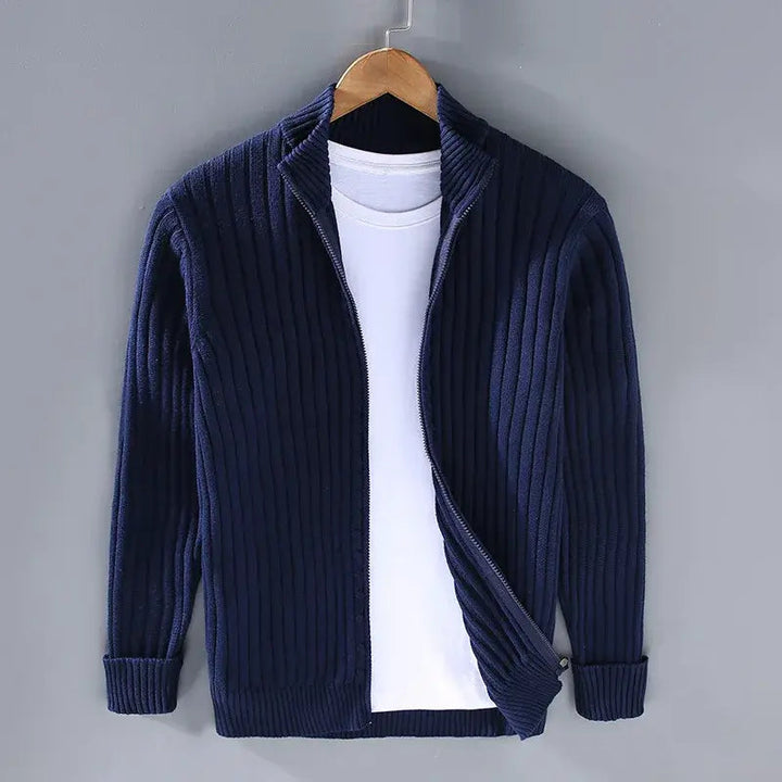 Cardigan blu scuro a coste con zip, appeso su gruccia, sopra maglietta bianca. Moda uomo, abbigliamento casual elegante, tessuto caldo.