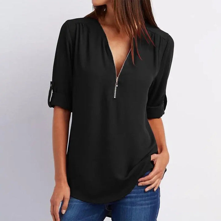 Blusa nera da donna con zip frontale, maniche lunghe arrotolate, scollo a V, abbinata a jeans blu. Moda casual elegante, abbigliamento femminile.