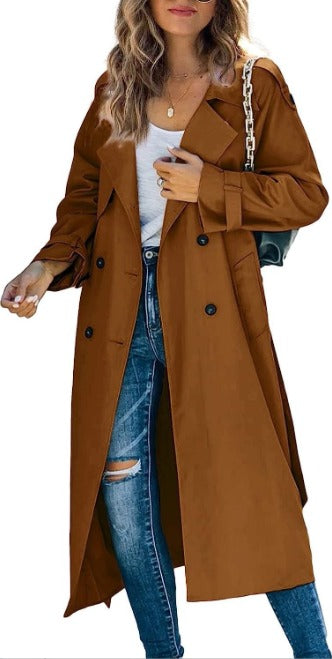 Cappotto lungo marrone da donna, stile trench, con bottoni neri, indossato su jeans strappati e maglietta bianca. Moda autunnale elegante.