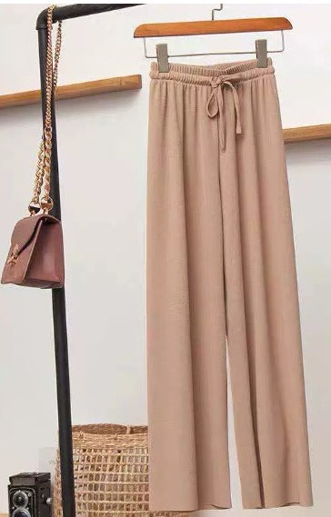Pantaloni beige a vita alta con cintura, appesi su appendiabiti, accanto a borsa marrone. Moda donna, abbigliamento casual elegante.