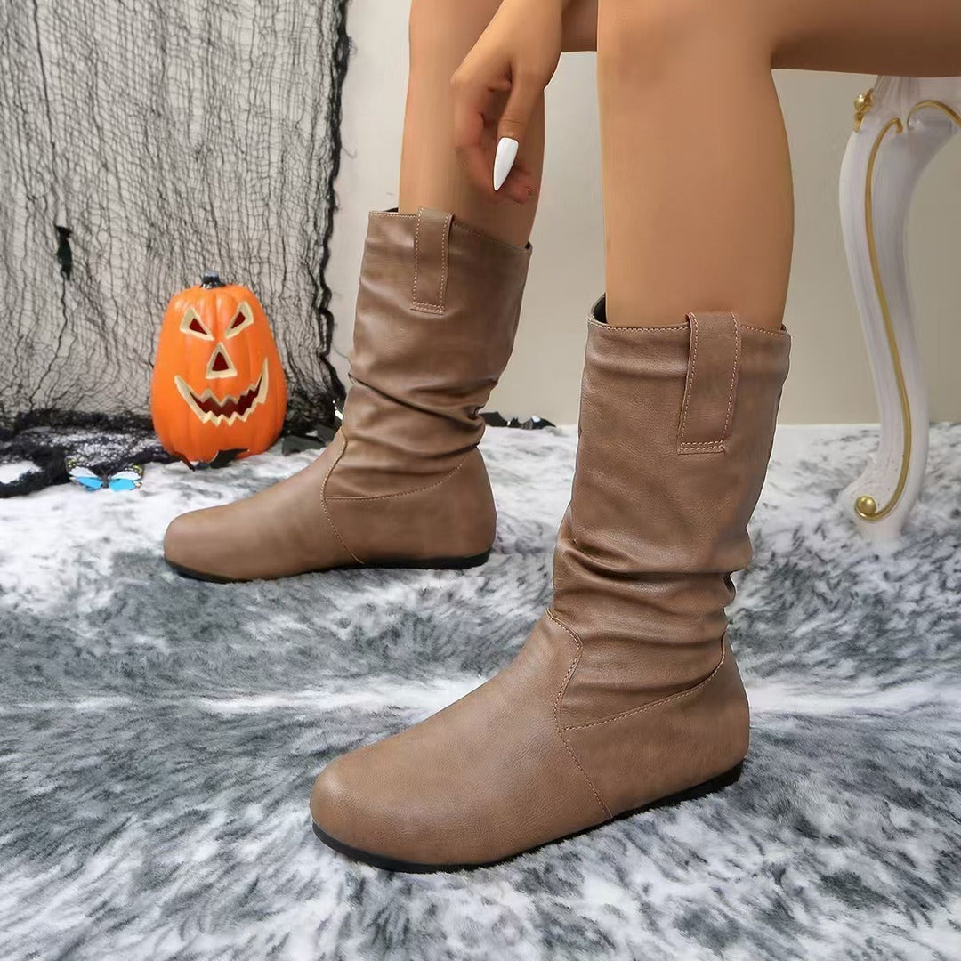 Stivali marroni in pelle su tappeto grigio, decorazione di Halloween con zucca intagliata sullo sfondo. Scarpe autunnali eleganti e comode.