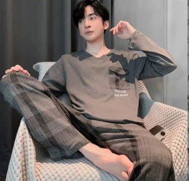 Giovane uomo in pigiama grigio a quadri seduto su poltrona, con smartphone accanto. Stile casual, relax domestico, moda uomo autunnale.