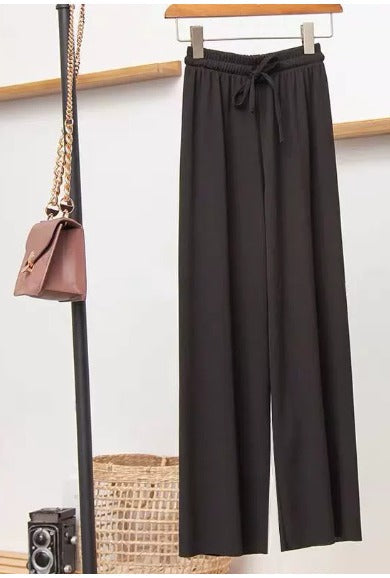 Pantaloni neri larghi appesi, borsa a tracolla marrone con catena dorata, fotocamera vintage e cesto intrecciato sullo sfondo.