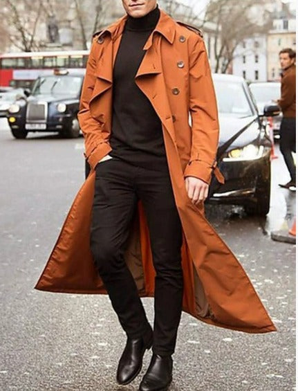 Uomo con trench marrone su strada cittadina, indossa dolcevita nero e pantaloni scuri. Moda autunnale, stile urbano elegante.