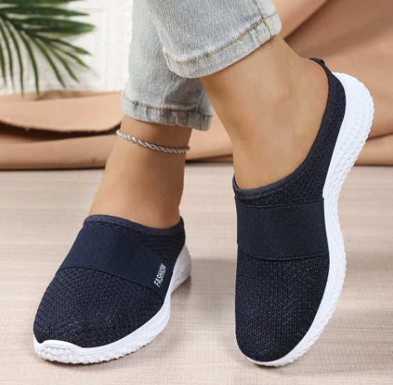 Scarpe slip-on blu scuro da donna, suola bianca, tessuto traspirante, indossate con jeans chiari. Calzature casual comode e alla moda.