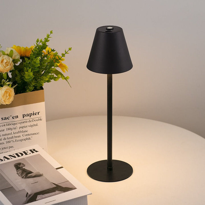 Lampada da tavolo nera moderna su tavolo bianco, accanto a fiori gialli e libri. Design minimalista, illuminazione interna elegante.