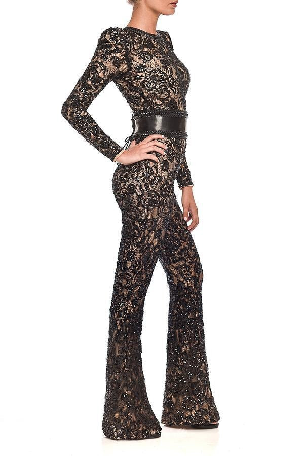 Tuta elegante in pizzo nero trasparente con cintura in pelle, maniche lunghe e pantaloni a zampa. Moda donna, abbigliamento da sera sofisticato.