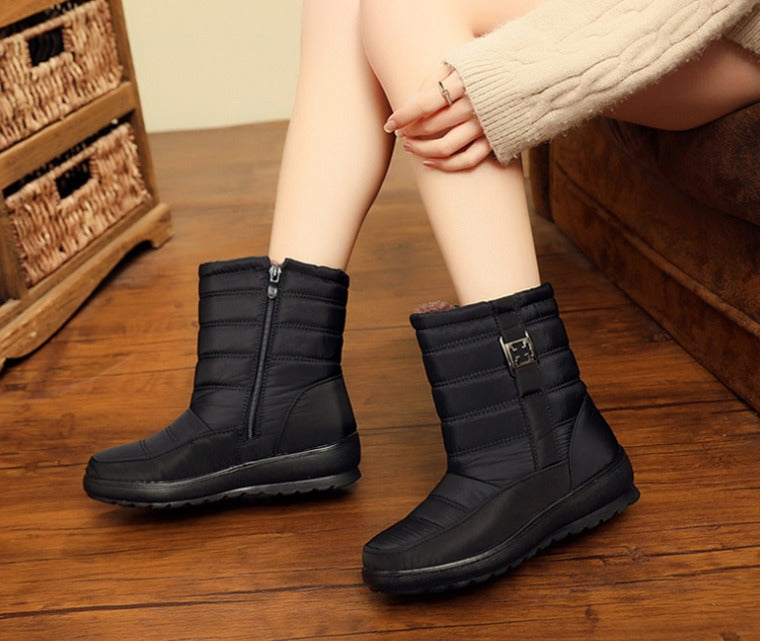 Stivali invernali neri da donna con cerniera, su pavimento in legno, indossati con maglione beige. Scarpe calde e impermeabili per l'inverno.