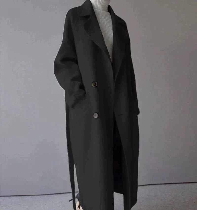 Cappotto lungo nero elegante, doppio petto, con cintura, indossato su maglione bianco. Moda autunnale, abbigliamento donna, stile minimalista.