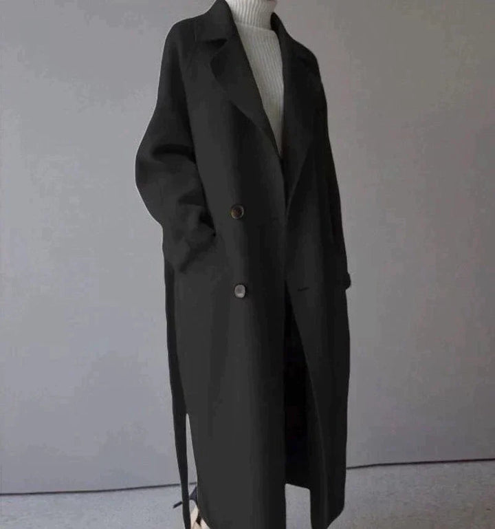 Cappotto lungo nero elegante, doppio petto, con cintura, indossato su maglione bianco. Moda autunnale, abbigliamento donna, stile minimalista.