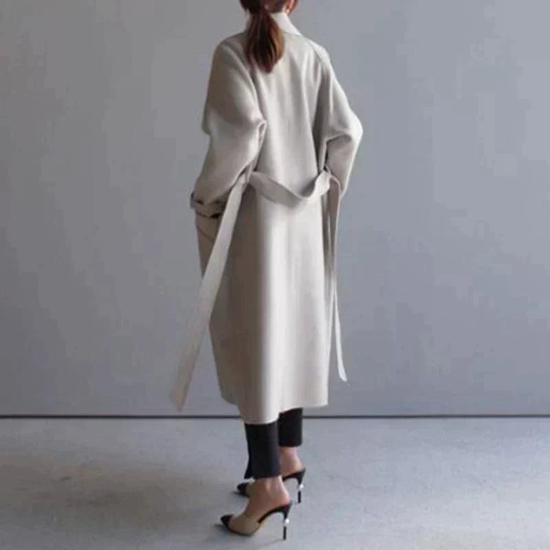 Cappotto lungo beige donna, design elegante, cintura in vita, abbinato a pantaloni neri e tacchi alti. Moda autunnale, stile minimalista.