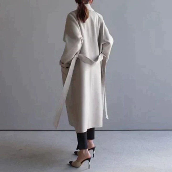 Cappotto lungo beige donna, design elegante, cintura in vita, abbinato a pantaloni neri e tacchi alti. Moda autunnale, stile minimalista.