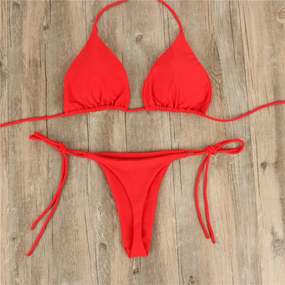 Bikini rosso a due pezzi su sfondo in legno, con top a triangolo e slip con laccetti. Costume da bagno estivo, moda mare donna.