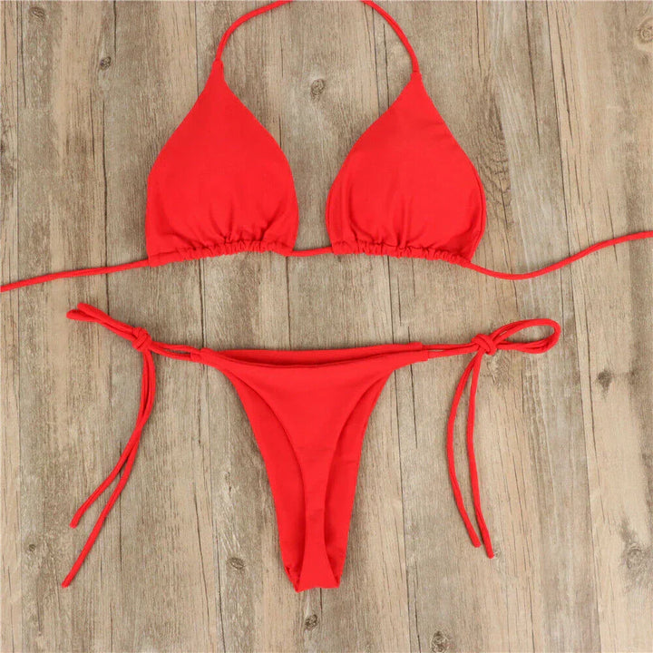 Bikini rosso a due pezzi su sfondo in legno, con top a triangolo e slip con laccetti. Costume da bagno estivo, moda mare donna.