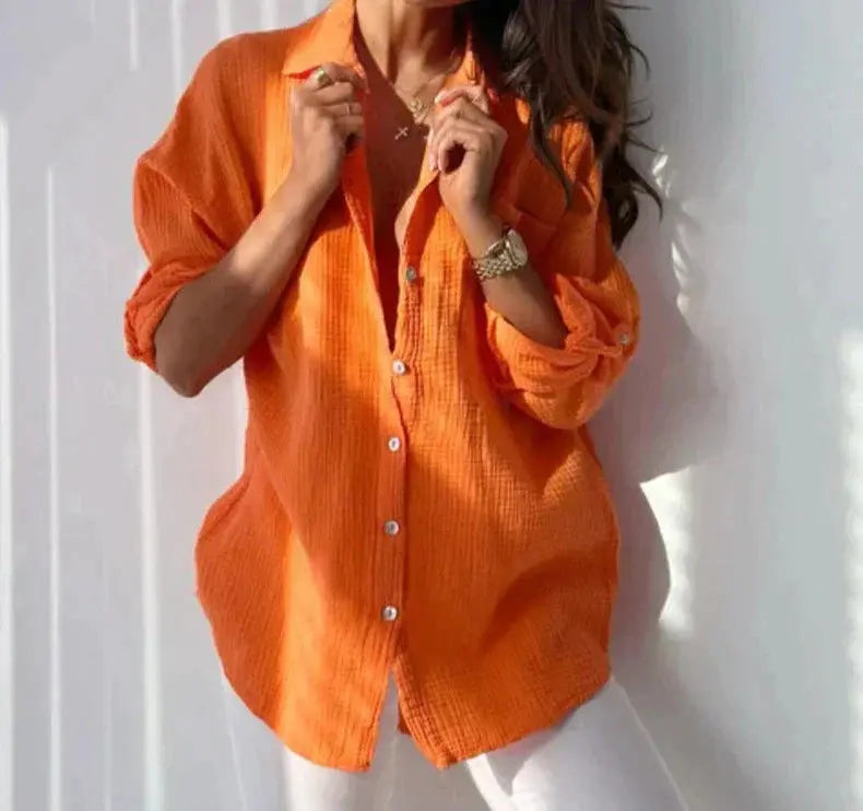 Camicia donna arancione a maniche lunghe, tessuto leggero, abbinata a pantaloni bianchi. Stile casual, moda femminile, abbigliamento estivo.
