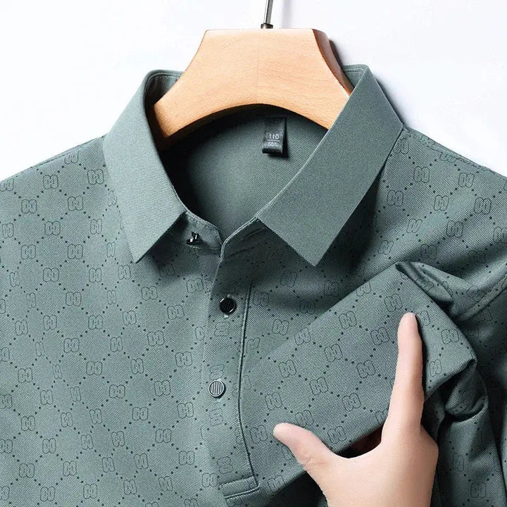 Camicia verde a maniche lunghe con motivo geometrico, colletto classico e bottoni, appesa su gruccia di legno. Tessuto elegante e moderno.