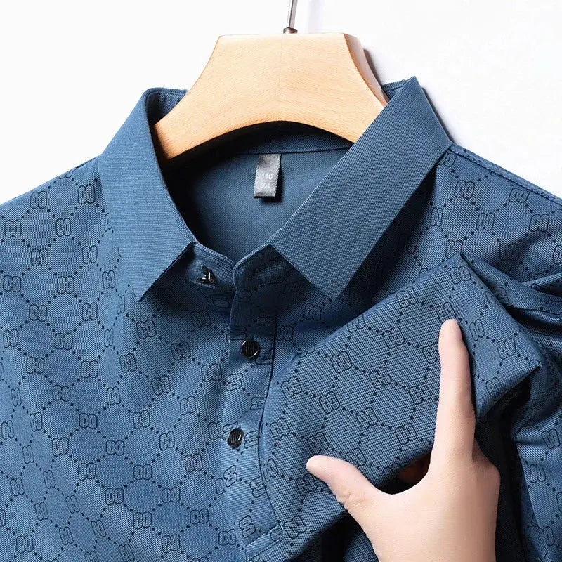 Camicia uomo blu con motivo geometrico, colletto classico e bottoni neri, appesa su gruccia di legno. Tessuto elegante e moderno.