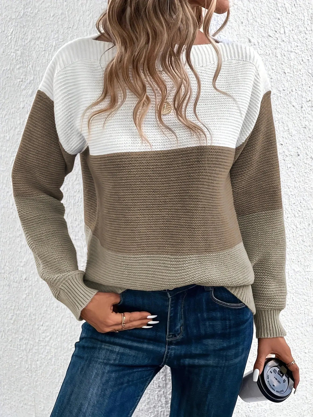 Maglione a righe bianche e marroni, donna con capelli ondulati, jeans blu, tiene una tazza. Moda autunnale casual, abbigliamento femminile trendy.