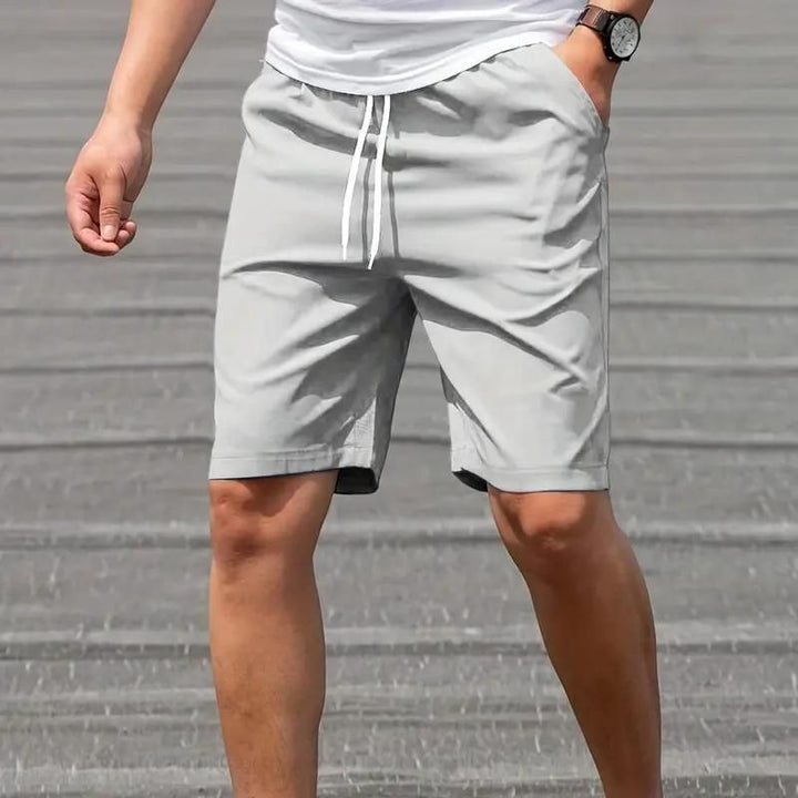 Pantaloncini sportivi grigi da uomo, con coulisse e tasche laterali, indossati con maglietta bianca. Ideali per attività sportive e tempo libero.