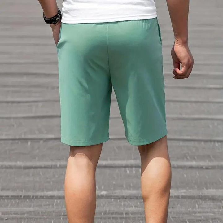 Pantaloncini sportivi verdi da uomo, tessuto leggero, indossati all'aperto. Ideali per attività fisica e tempo libero.