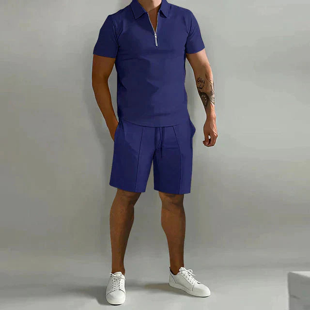 Completo estivo uomo blu, polo con zip e pantaloncini, stile casual, tessuto leggero, ideale per moda estiva, abbinato a scarpe bianche.