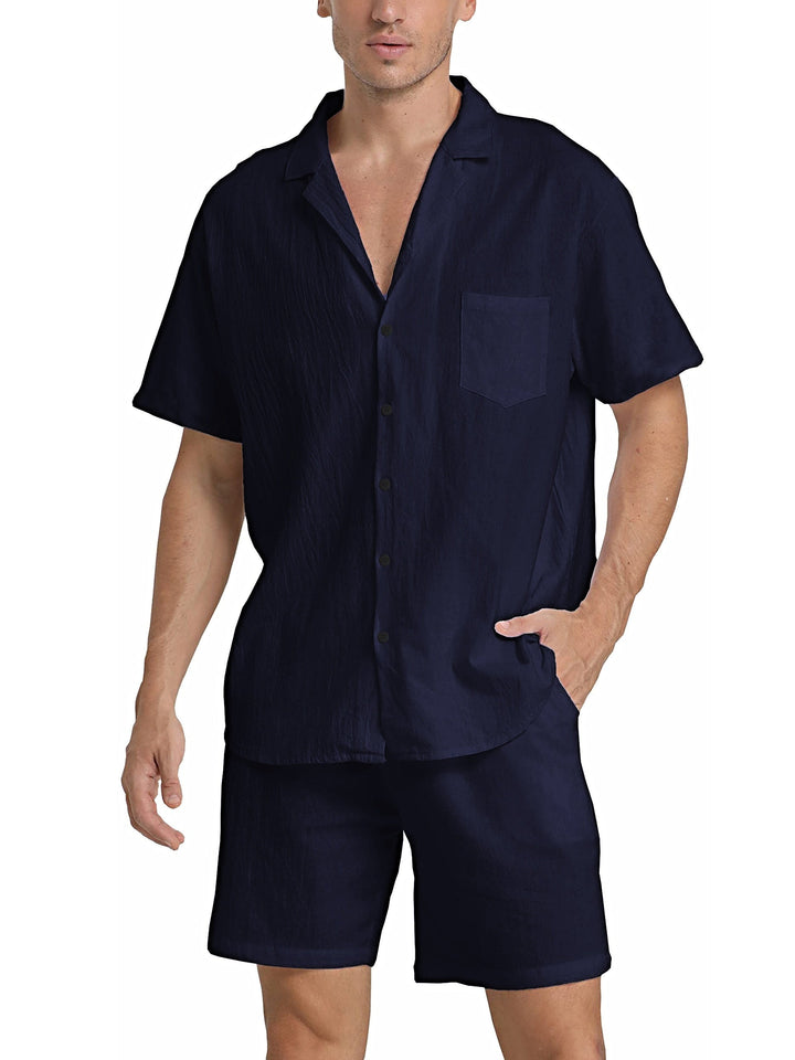 Uomo in completo estivo blu scuro, camicia a maniche corte con colletto e taschino, pantaloncini coordinati. Moda maschile casual elegante.