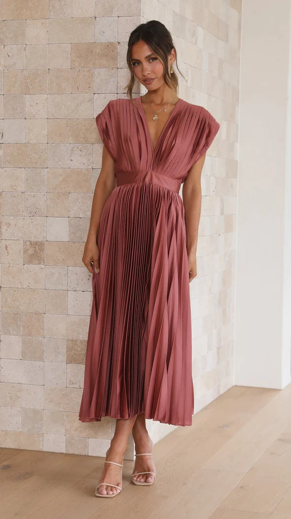 Abito lungo plissettato rosa antico, scollo a V profondo, maniche corte, indossato da donna in sandali beige. Elegante moda femminile estiva.