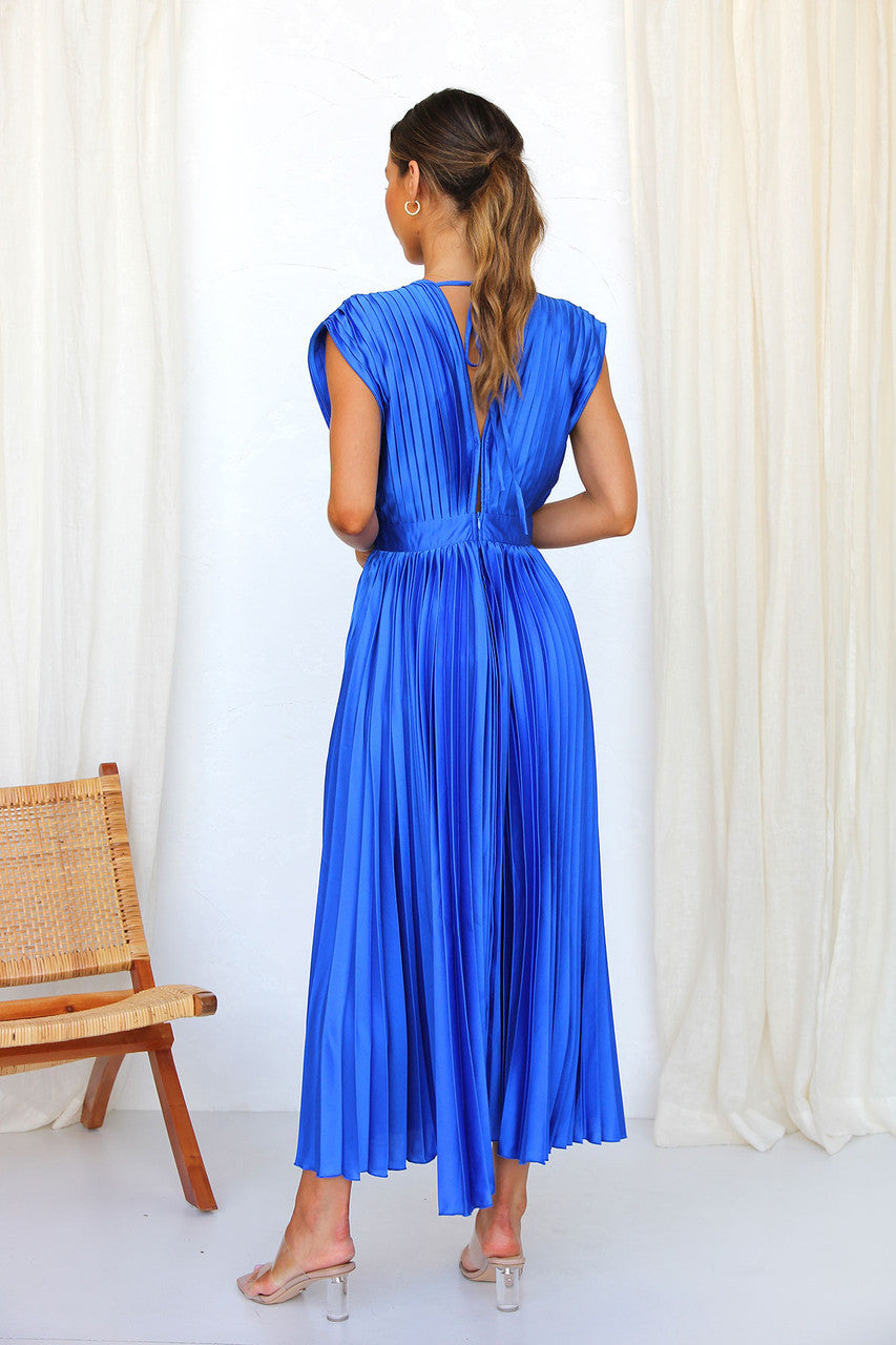 Abito lungo plissettato blu elettrico, donna di spalle, tessuto satinato, design elegante, perfetto per eventi formali, moda femminile contemporanea.