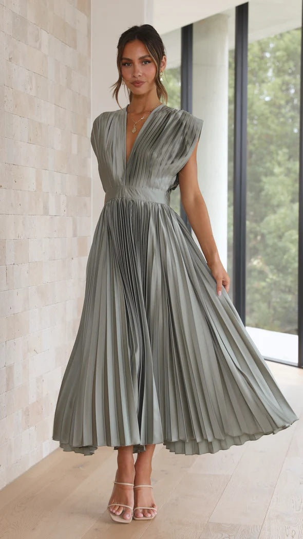 Abito lungo plissettato grigio elegante, senza maniche, indossato da una donna in interni moderni. Perfetto per eventi formali e cerimonie.