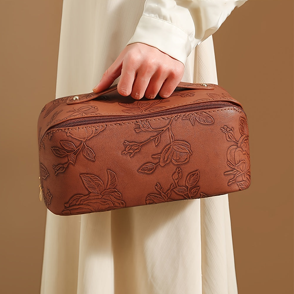 Borsa a mano in pelle marrone con motivo floreale in rilievo, chiusura a zip, tenuta da una persona in abito bianco. Accessorio moda elegante.