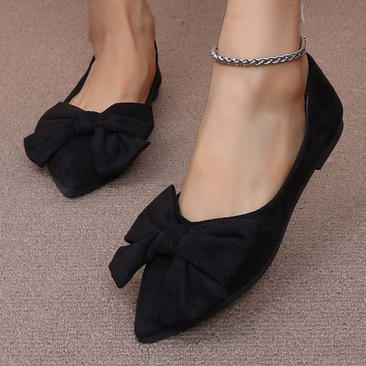 Scarpe ballerine nere da donna con fiocco, indossate su tappeto beige. Eleganti e comode, ideali per moda casual e formale.