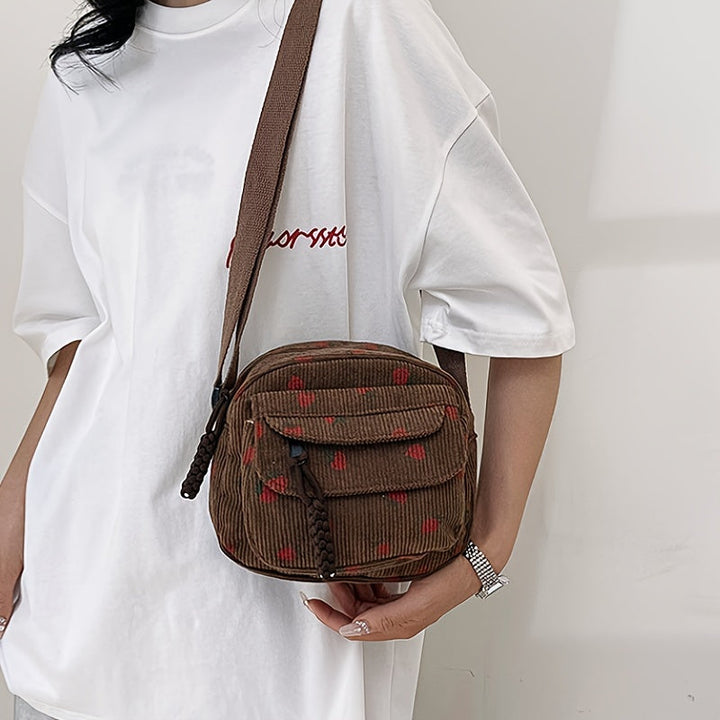 Donna con borsa a tracolla marrone in velluto a coste, motivo floreale rosso, indossa t-shirt bianca. Accessorio moda casual, stile urbano.