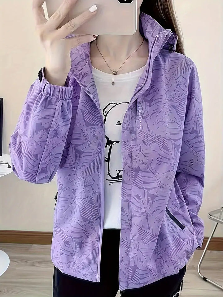 Giacca a vento viola con motivo floreale, indossata da una donna. Design casual, ideale per la moda autunnale. Tasche laterali e cerniera frontale.