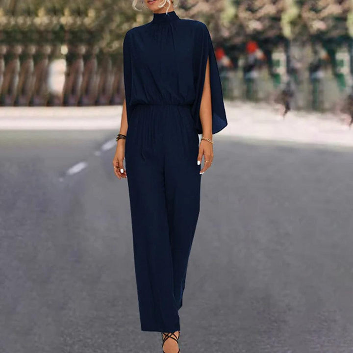 Tuta elegante blu scuro con mantella, donna in strada alberata. Abbigliamento moda femminile, stile sofisticato, tendenza autunno.
