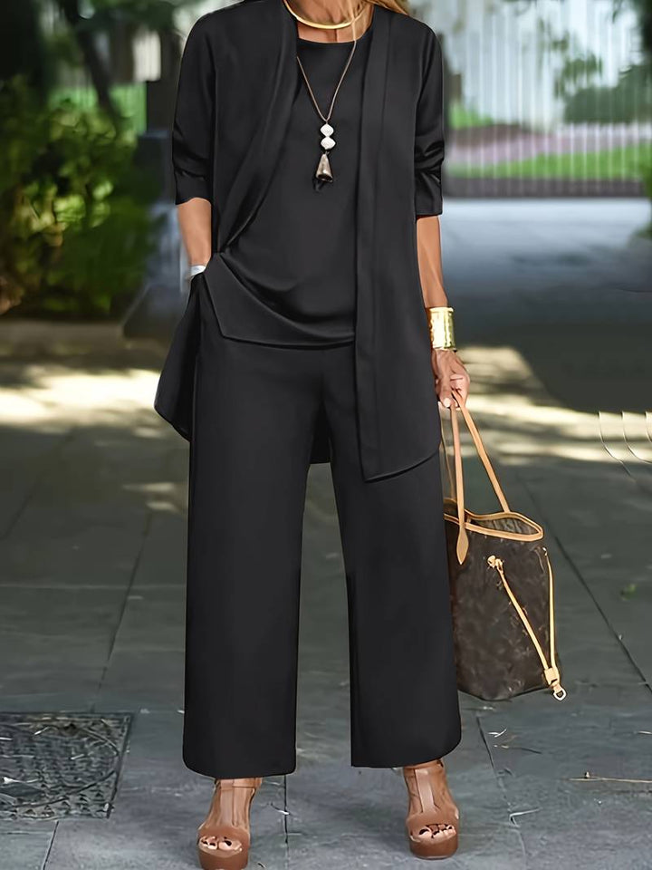Donna in elegante completo nero, pantaloni larghi e giacca, con borsa di lusso marrone e sandali con zeppa. Look moda urbana chic.