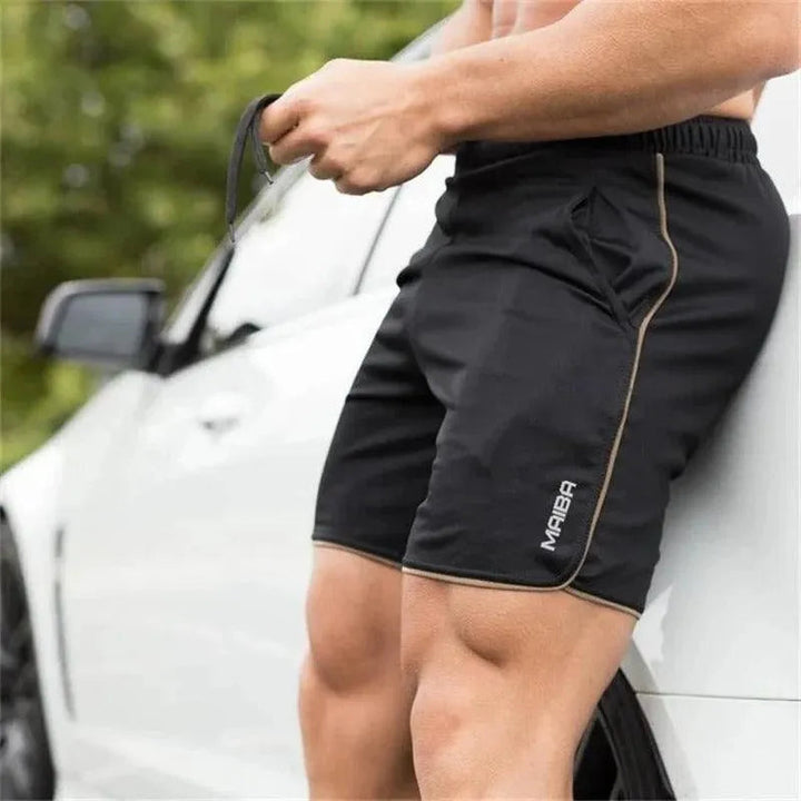 Uomo in pantaloncini sportivi neri NABBA, appoggiato a un'auto bianca. Abbigliamento fitness maschile, moda sportiva, attività all'aperto.