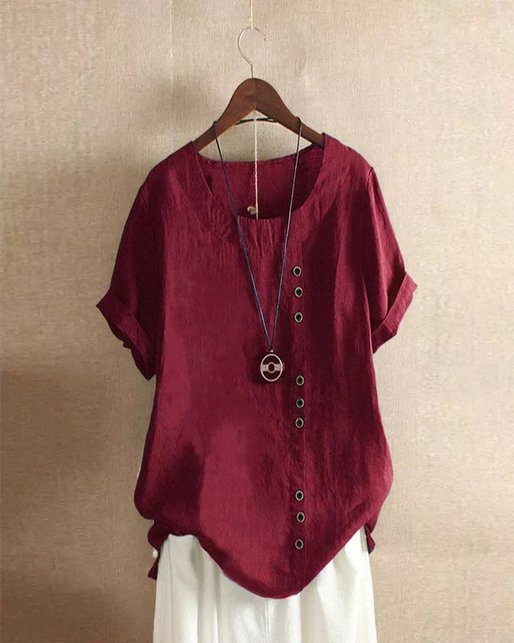 Blusa rossa in lino con bottoni decorativi, maniche corte, scollo rotondo, appesa su gruccia. Moda donna estiva casual elegante.