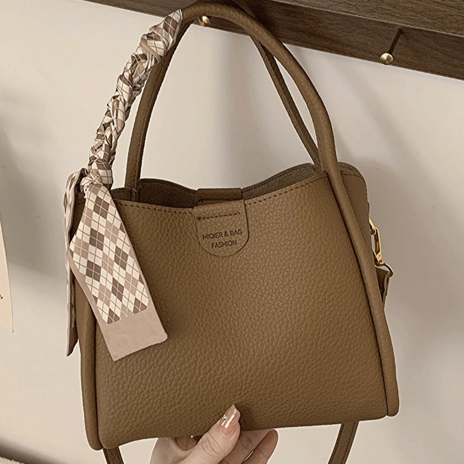 Borsa a mano in pelle marrone con manico intrecciato e foulard decorativo, design elegante e moderno, ideale per moda femminile e accessori di lusso.
