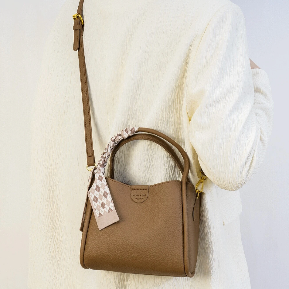 Borsa a tracolla marrone in pelle, indossata su spalla, con foulard decorativo. Elegante accessorio moda donna, perfetto per ogni occasione.